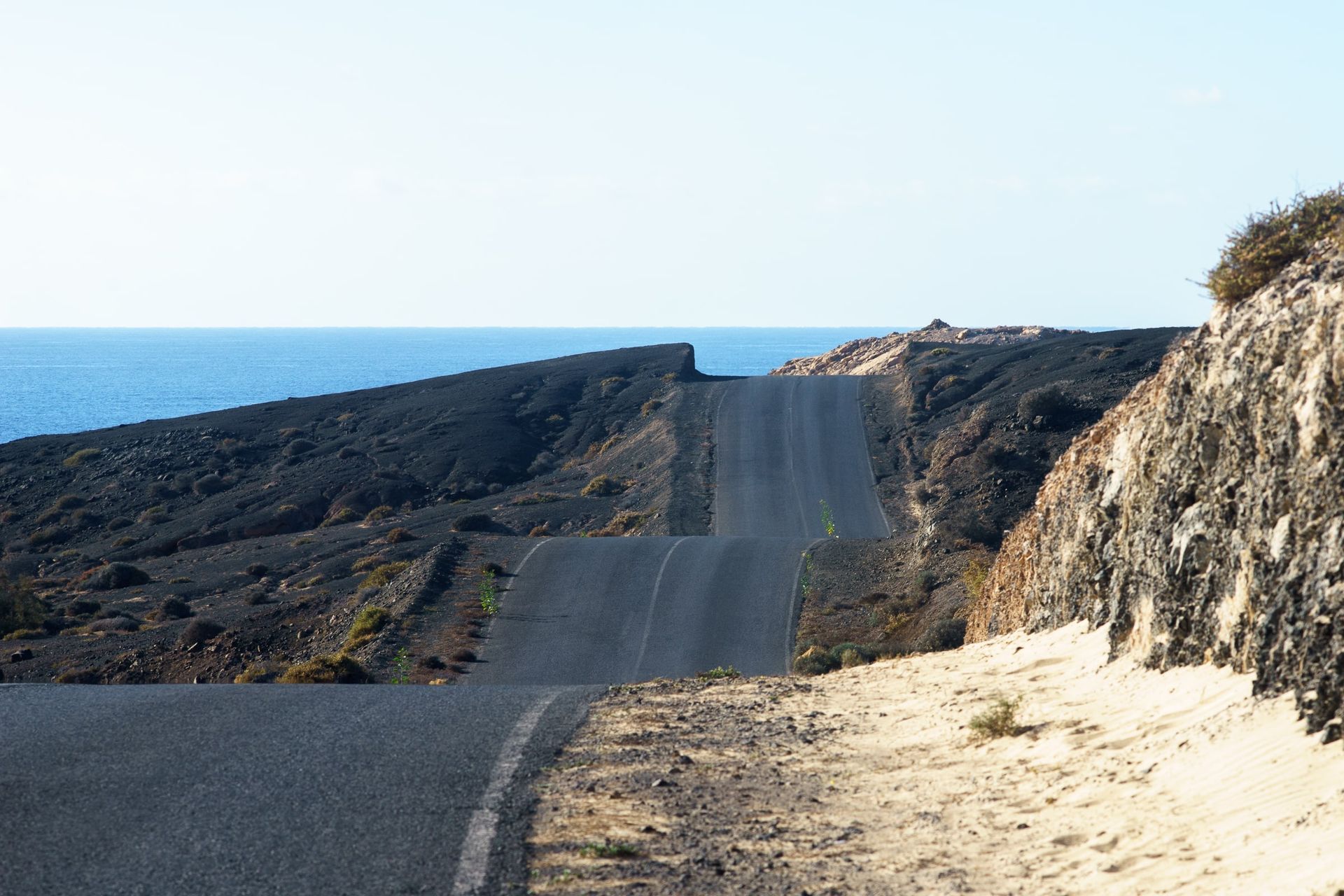 Geschwungene Straße durch die Vulkanlandschaft Fuerteventuras, die zum Meer führt